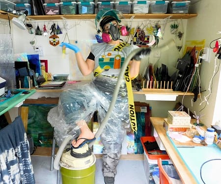 Mountain Woman Products Stained Glass Artist wrapped in plastic covered in safety gear holding a vacuum